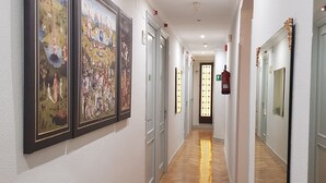 Un pasillo con suelo de madera, paredes blancas y cuadros en la pared izquierda.