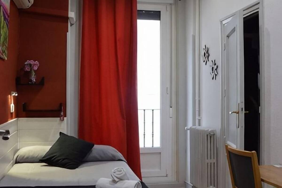 A bedroom with a bed, a window with a view, a radiator, and a door.