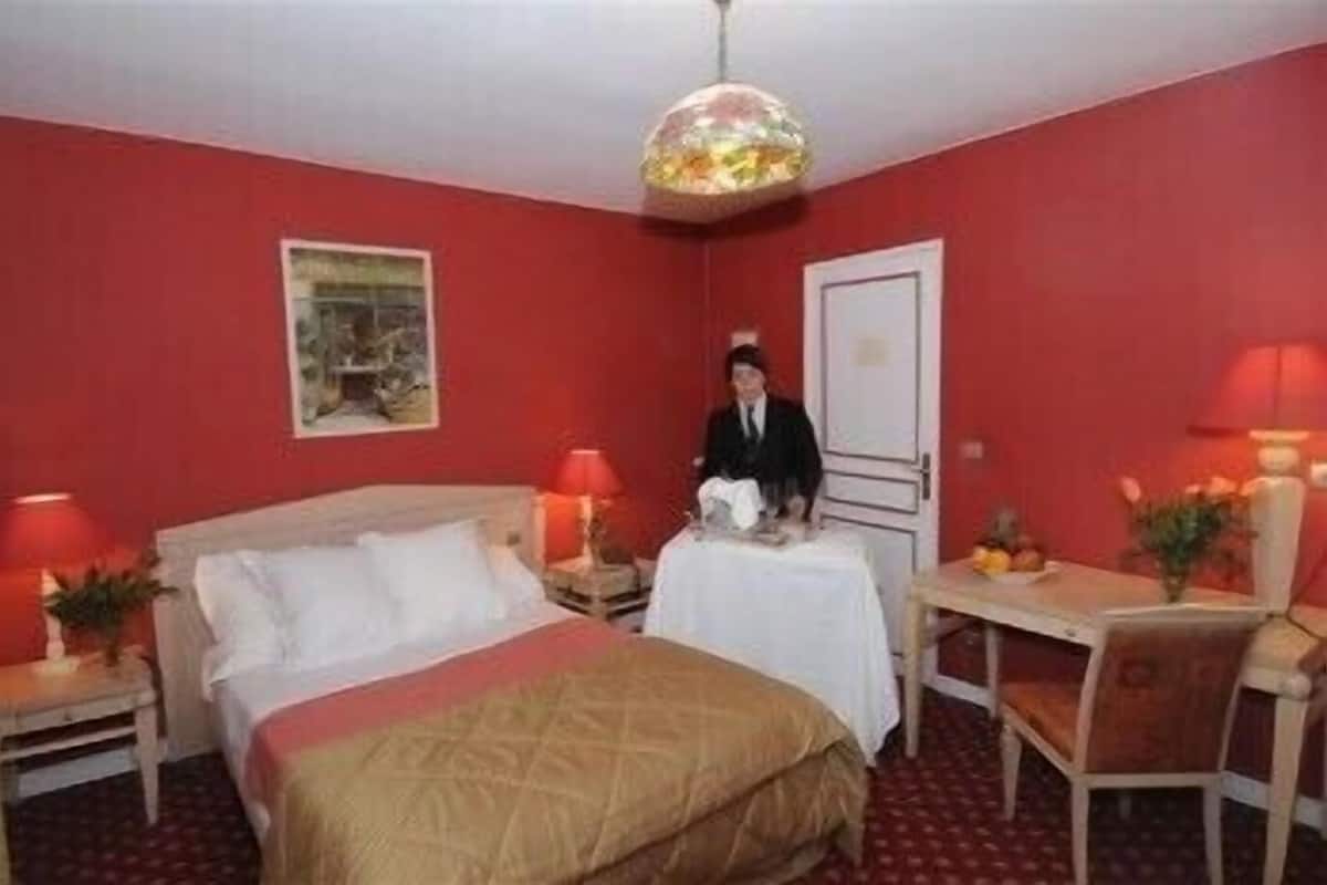 A hotel room with a bed, a desk, a chair, a nightstand, and a hanging light fixture.