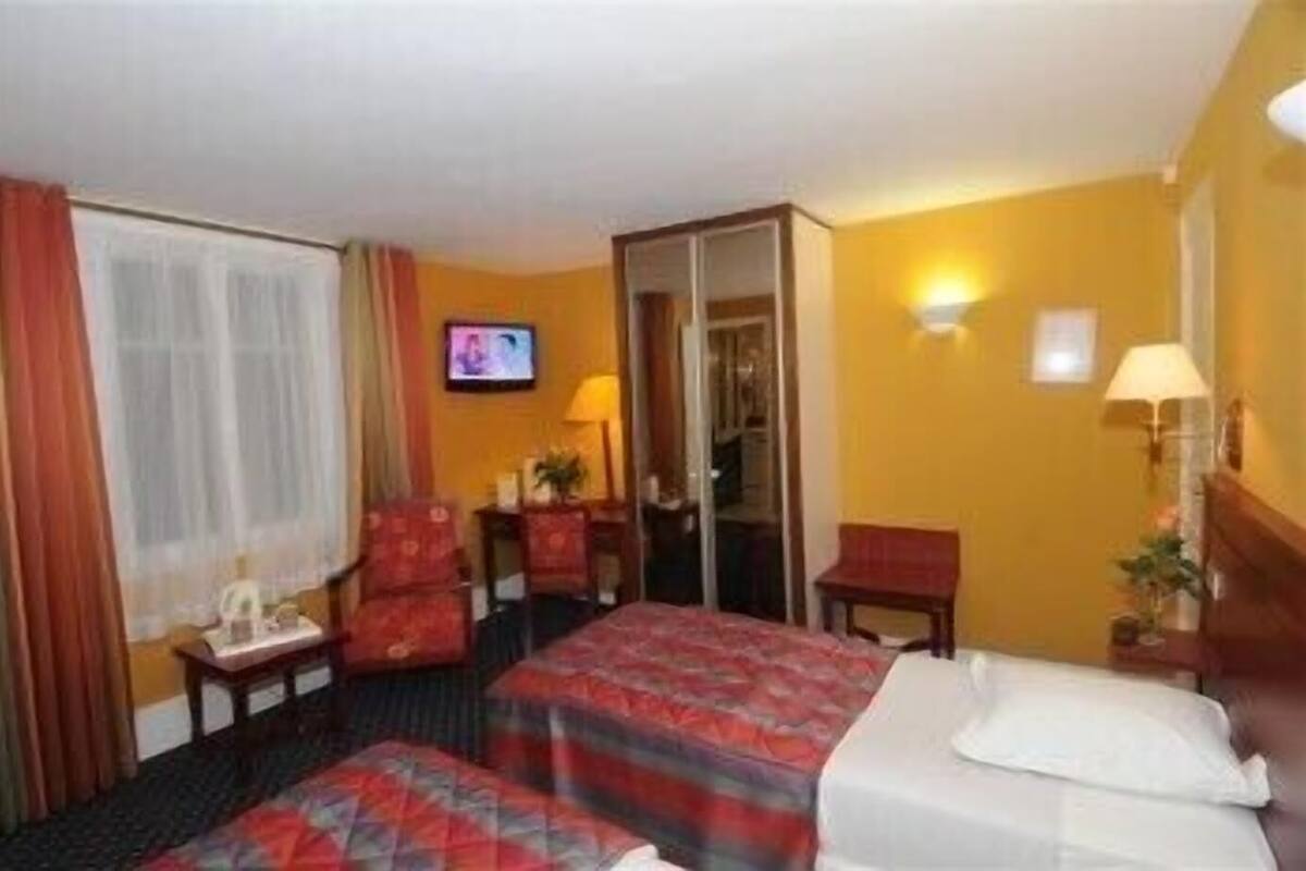 A hotel room with two beds, a television, a desk, a chair, and a mirror.