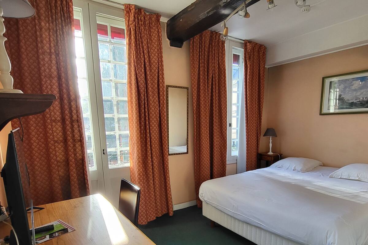 A hotel room with a bed, a desk with a lamp, a chair, and a window with curtains.