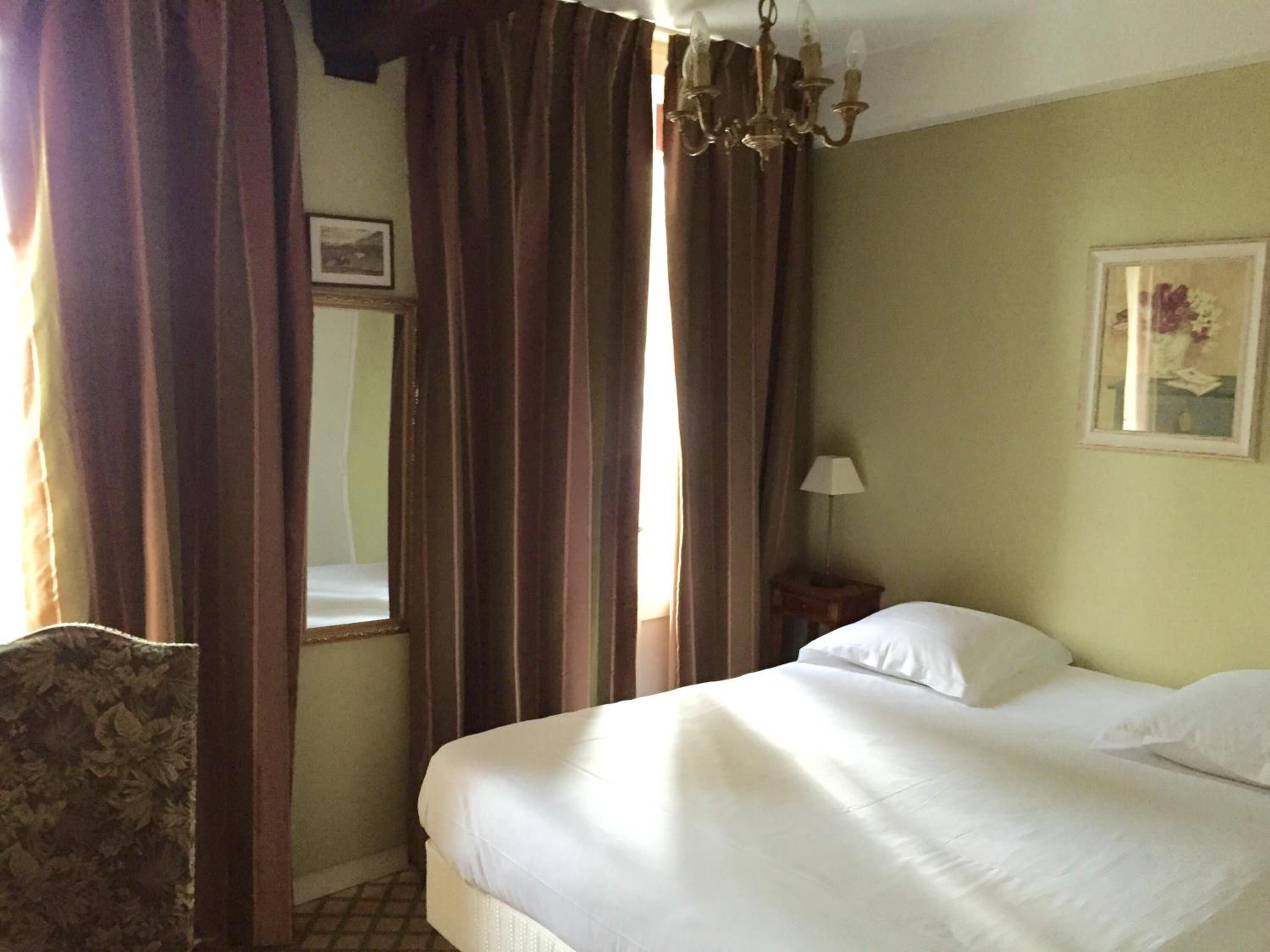 Una camera d'albergo con un letto, tende, un lampadario, un comodino e un quadro appeso al muro.