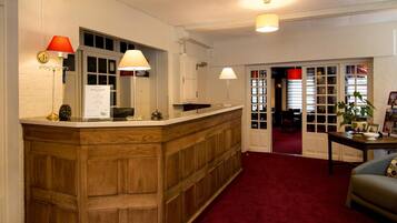A reception area with a wooden counter, two lamps, a sign, and a red carpet.