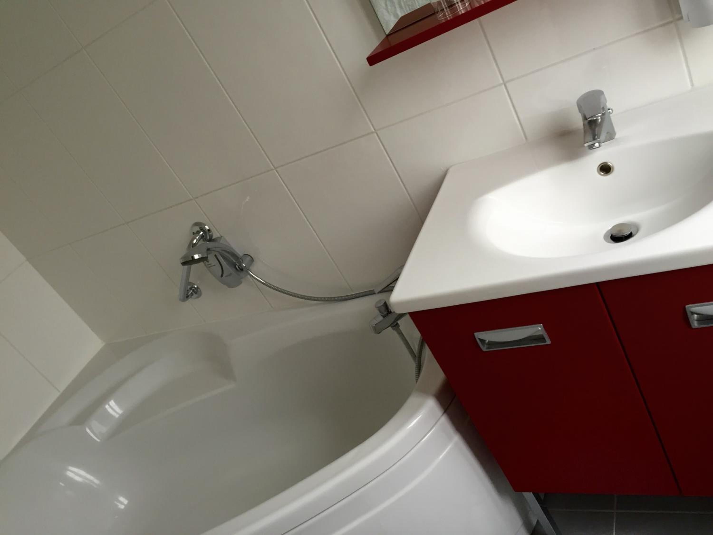 A bathroom with a white bathtub, a white sink, and red cabinets.