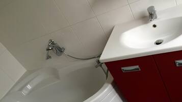A bathroom with a white bathtub, a white sink, and red cabinets.