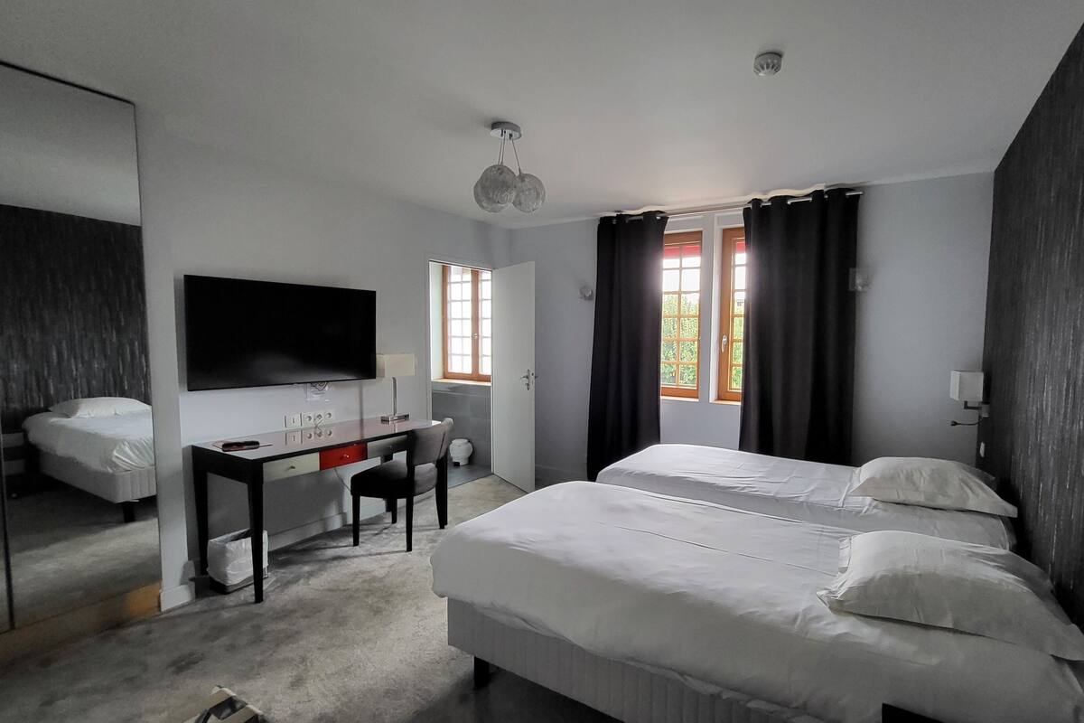 A modern hotel room with a large bed, a desk with a chair, a flat-screen TV, and a window with curtains.