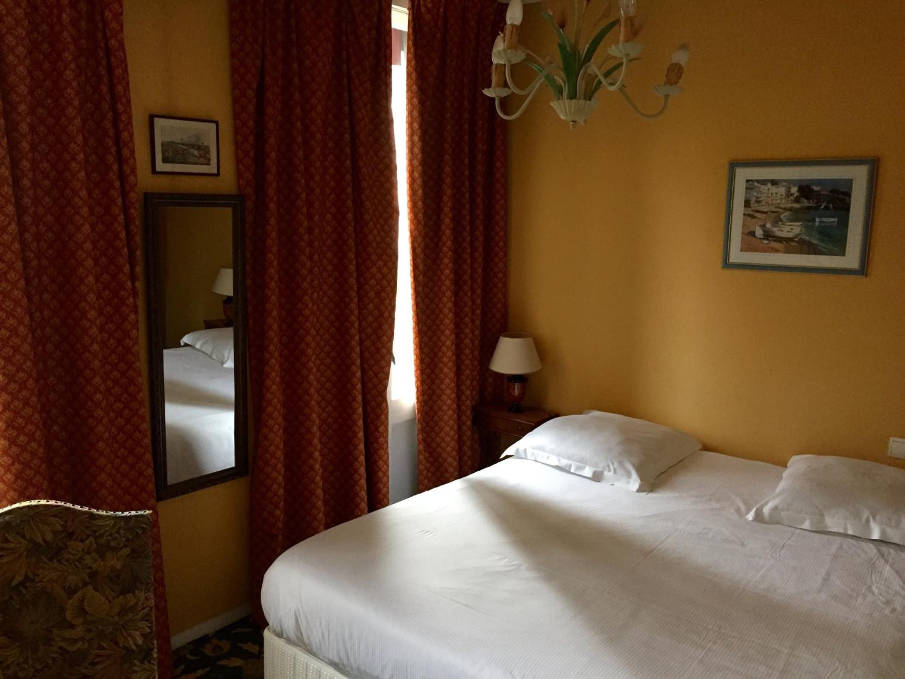 Ein Hotelzimmer mit Bett, Nachttisch, Lampe, Spiegel und einem Gemälde an der Wand.