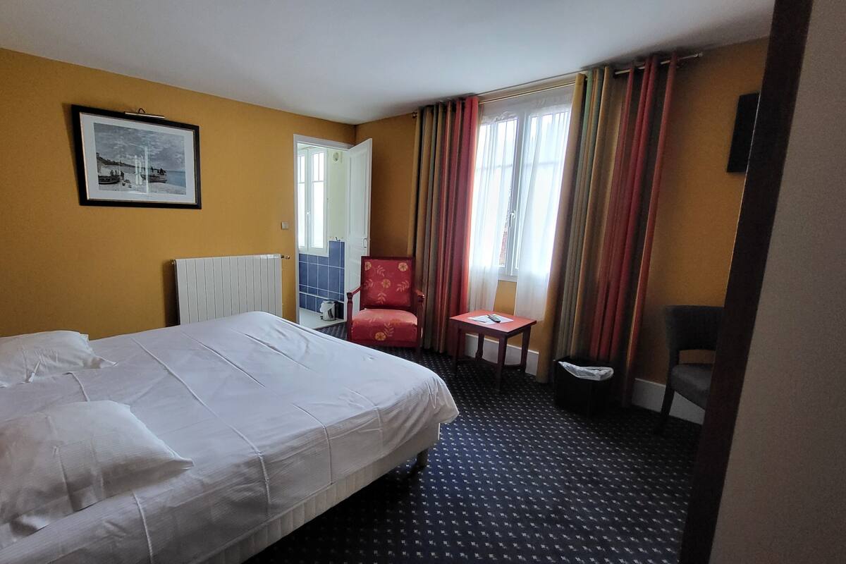 A hotel room with a large bed, a chair, a small table, a picture on the wall, and a window with curtains.