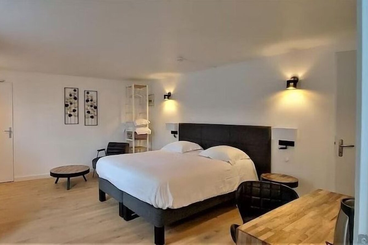 Una habitación de hotel con cama, mesitas de noche, una silla, una pequeña mesa y luces fijadas a la pared.
