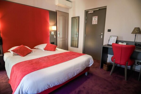A hotel room with a large bed, a desk, a chair, and a door. - Hôtel d'Angleterre (Saint-Calais)