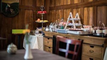 A wooden-paneled room with a buffet setup featuring a fruit display, a beverage station, and a tiered cake stand.