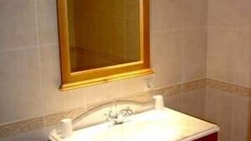 Un baño con tocador de madera, un lavabo blanco y un espejo con marco de madera.