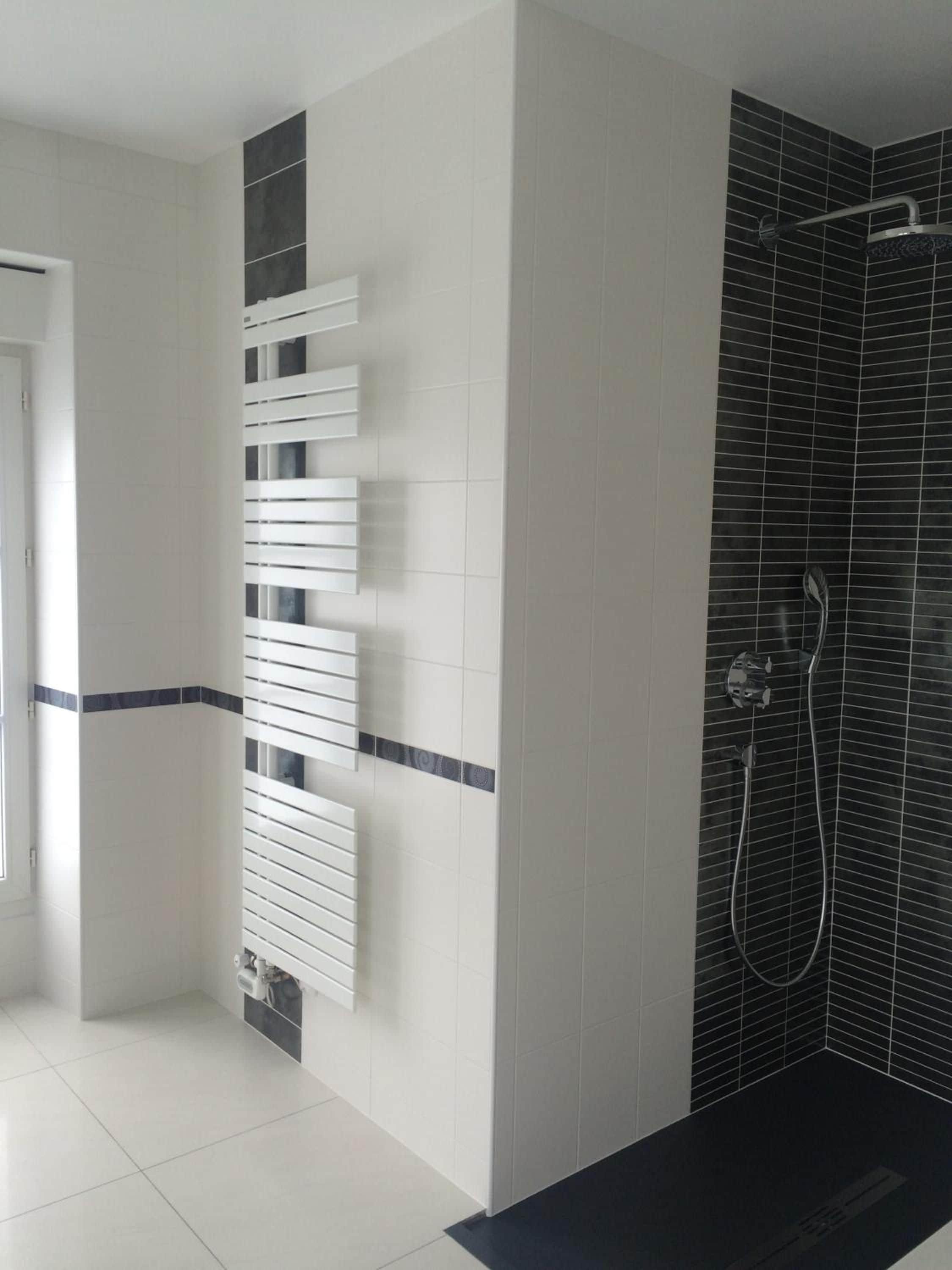 Ein modernes Badezimmer mit Dusche, weißen Fliesen an den Wänden und einer Duschfläche mit schwarzen Fliesen.
