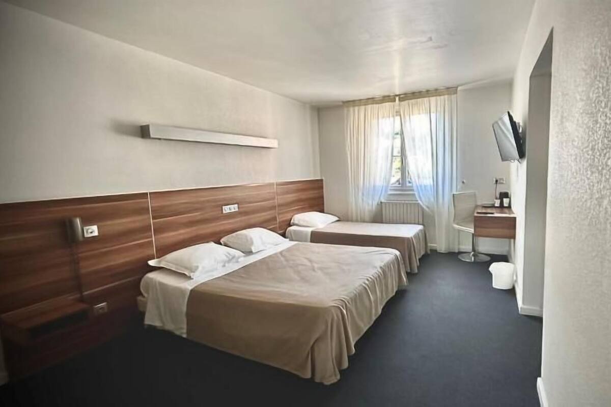 A hotel room with two beds, a desk, a TV, and a window with curtains.