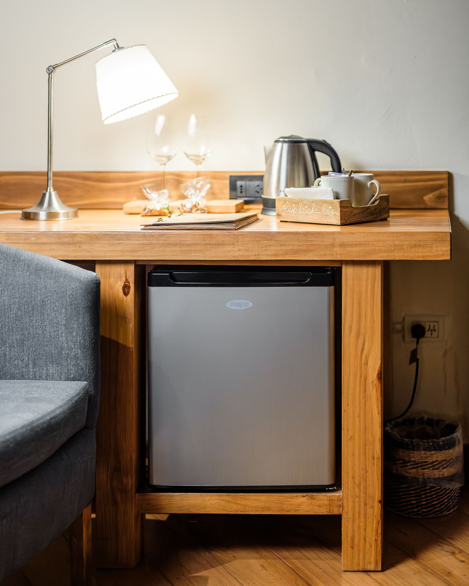 Une petite cuisine équipée avec un plan de travail en bois, un petit réfrigérateur, une machine à café et une lampe.