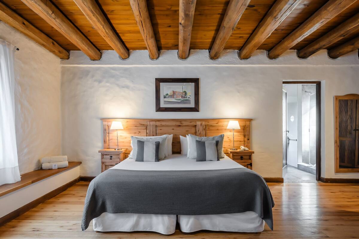 Ein Schlafzimmer mit Holzboden, einem Bett mit grauer Bettwäsche, zwei Nachttischen mit Lampen und einem gerahmten Bild an der Wand.