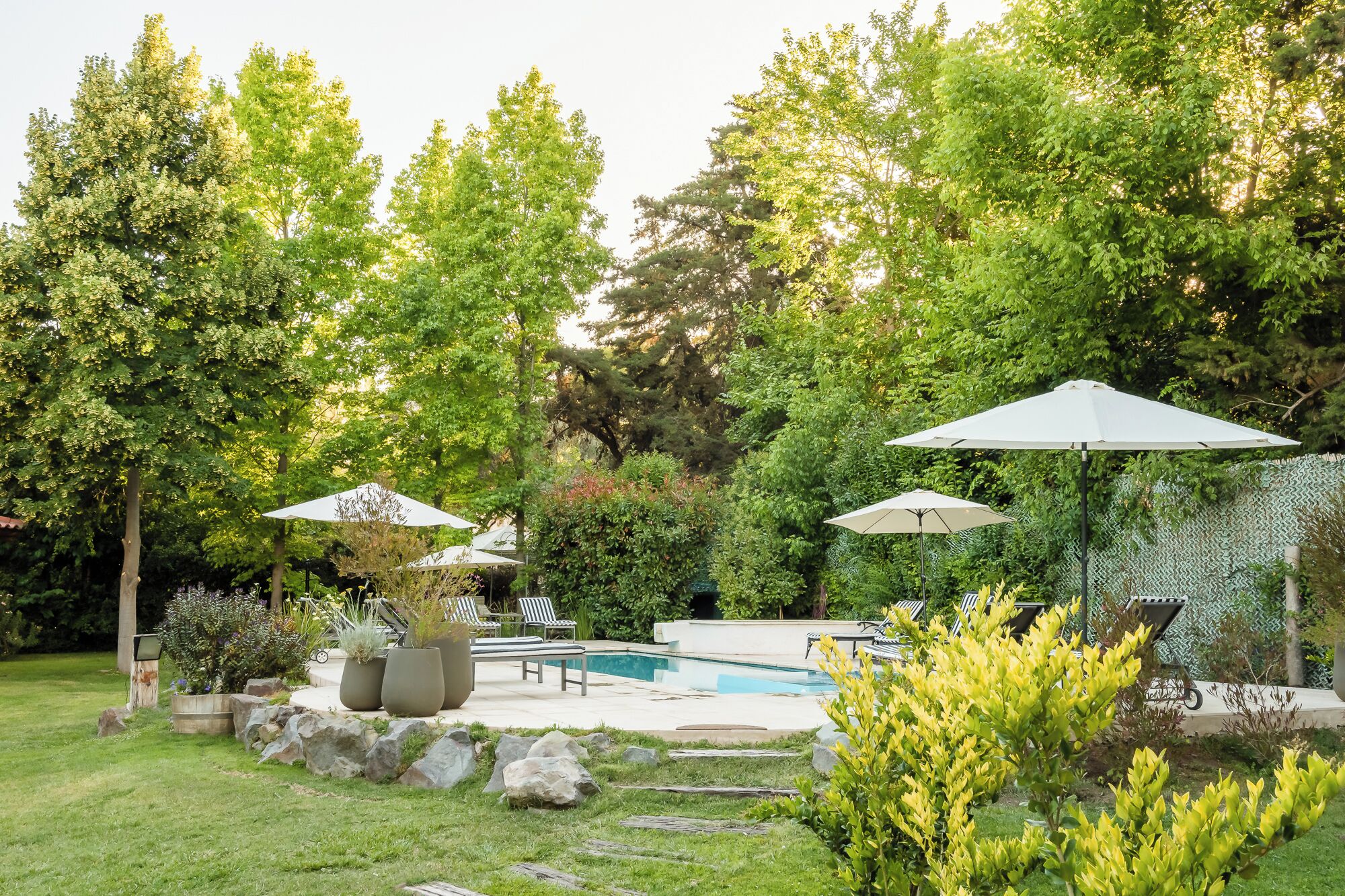 Un patio trasero con piscina, sillas de descanso y sombrillas.