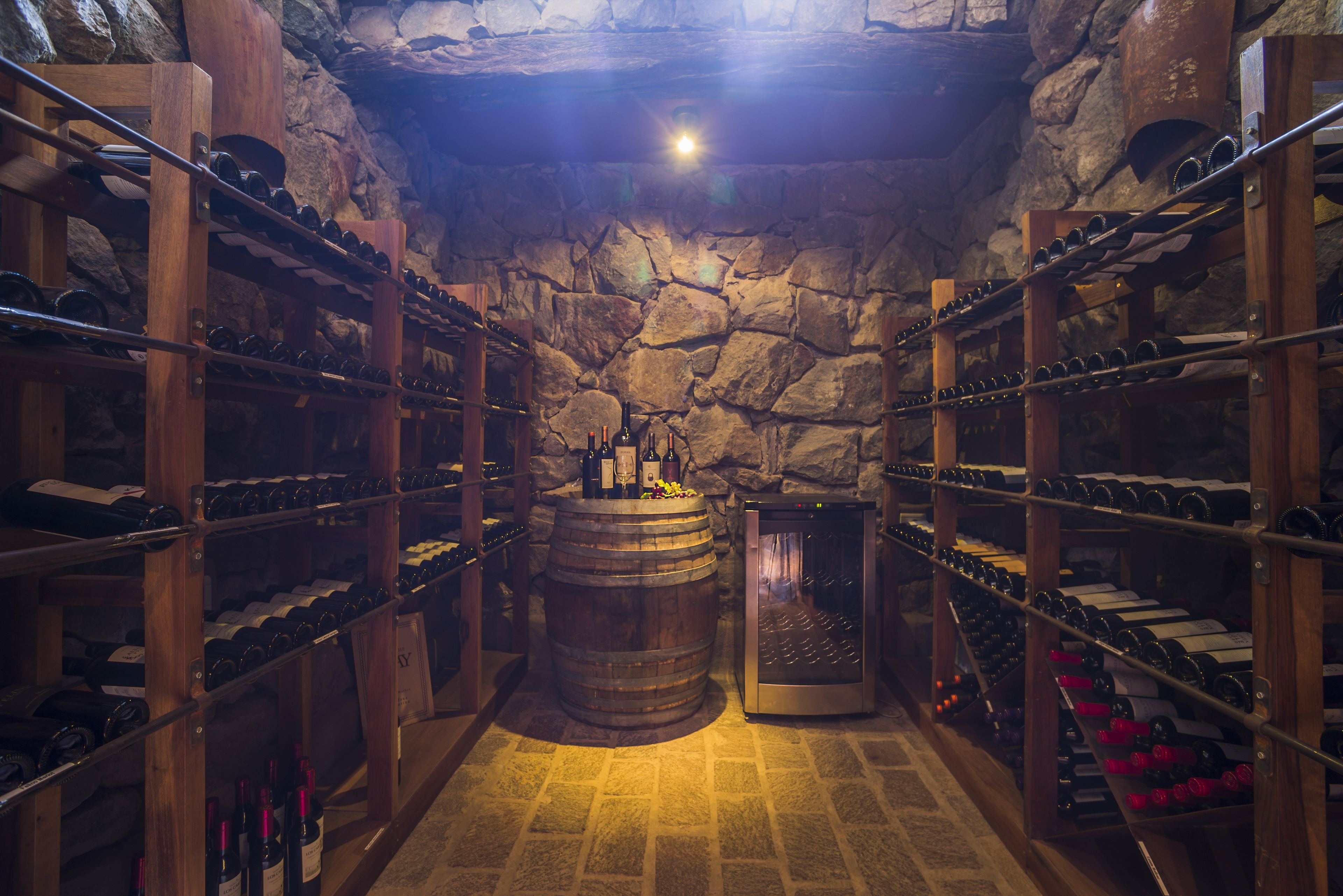 Una celler de vi amb prestatges de fusta, un barril gran, parets de pedra i un sòl de rajola.