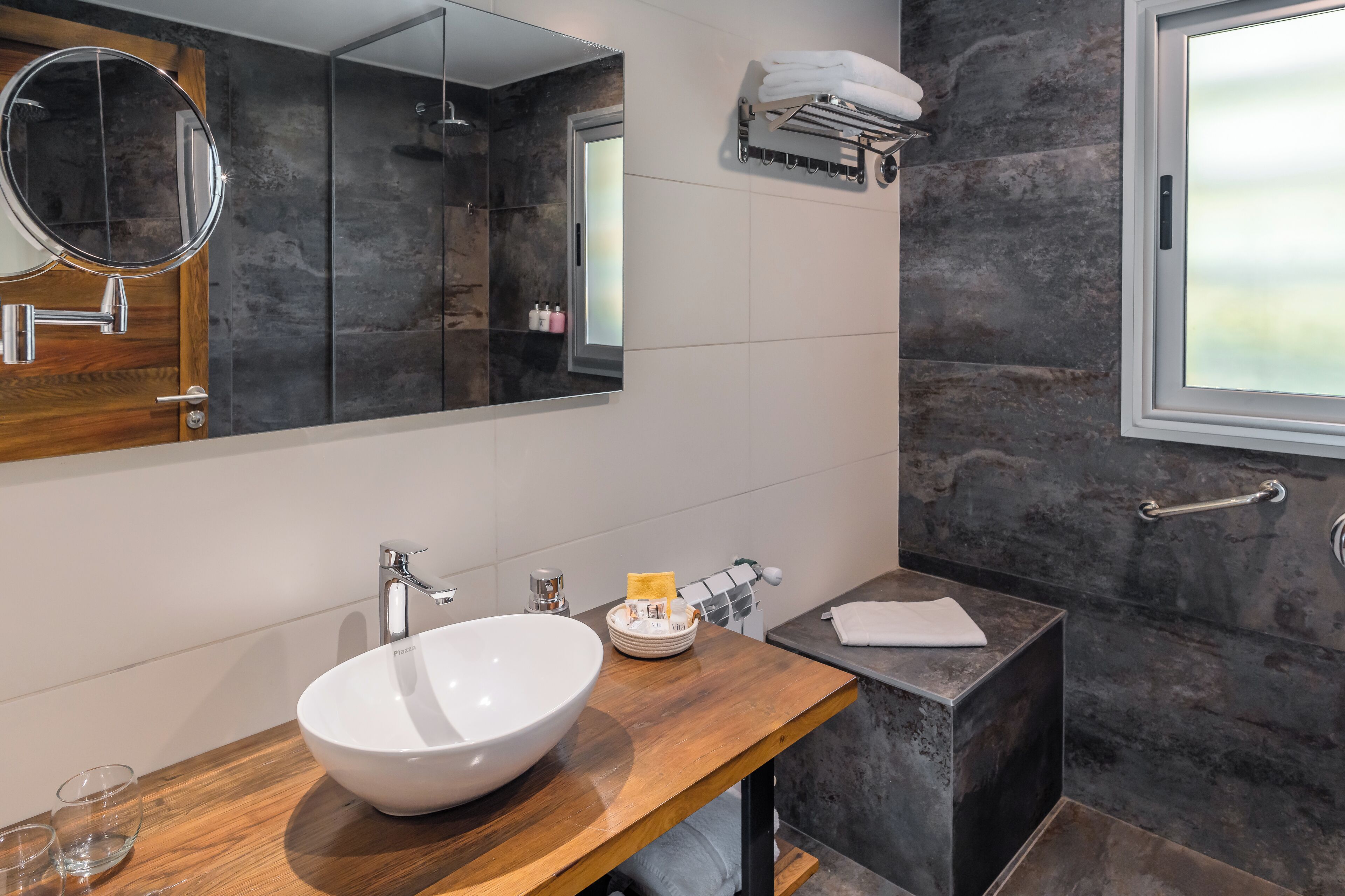 Un baño moderno con tocador de madera, un espejo grande, un lavabo blanco y una zona de ducha.