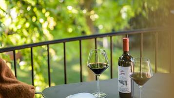 Una mesa con un libro, dos copas de vino y una botella de vino en un balcón con barandilla.