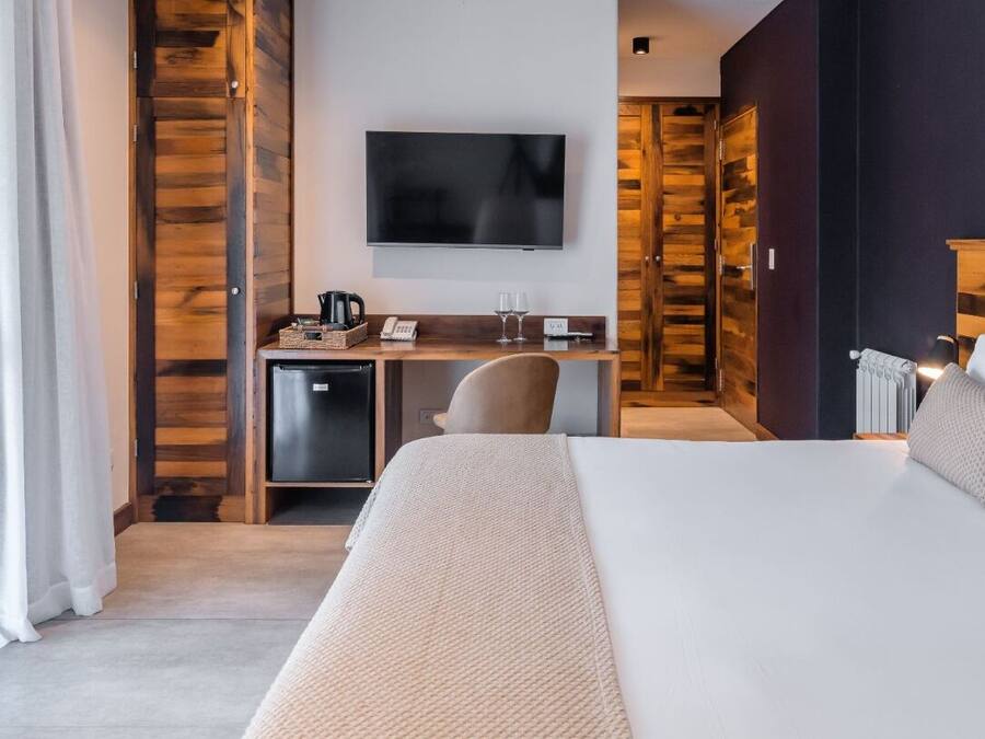 Een hotelkamer met een groot bed, een bureau met een computer, een aan de muur bevestigde televisie en een houten garderobe.