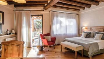 Una habitación de hotel acogedora con techo de madera, una cama con cubrecama gris, una silla roja, una mesa de madera y vistas al exterior a través de una ventana.