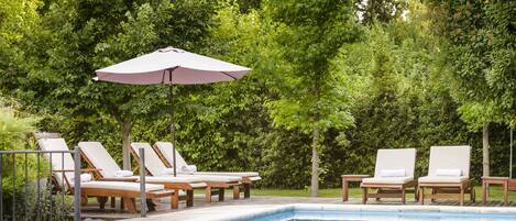 Un área junto a la piscina con sillones de descanso y una pérgola.