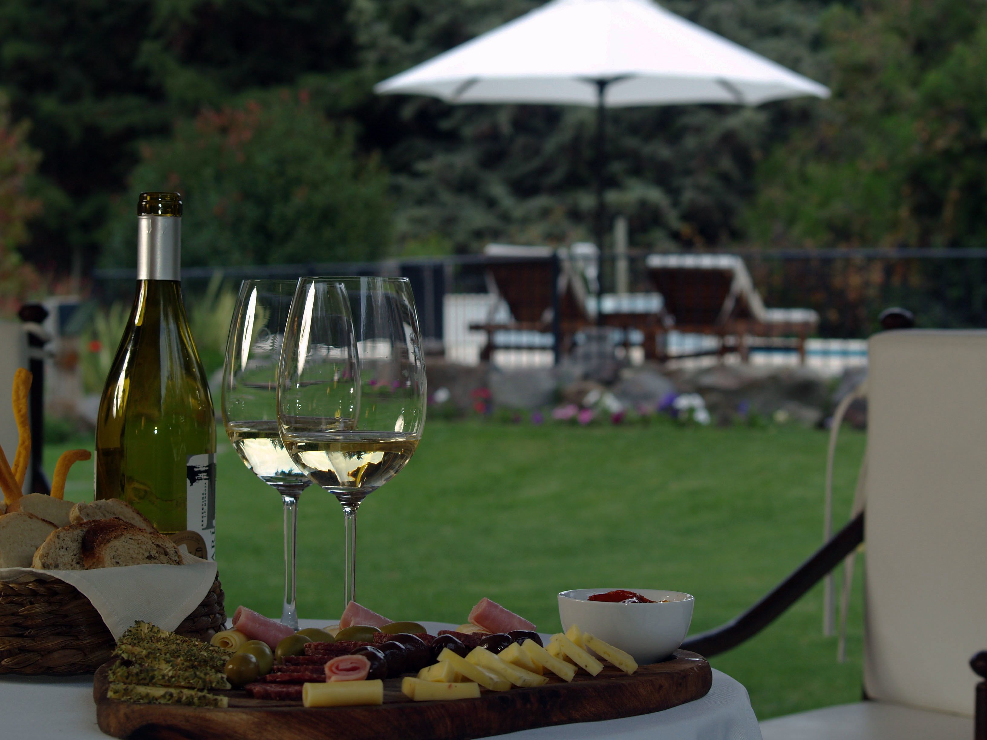 Une table avec une bouteille de vin, deux verres, une planche en bois sur laquelle sont disposés différents fromages et différentes sortes de charcuterie, et un bol de sauce.