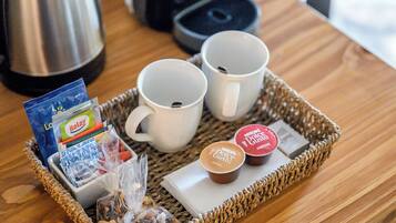 Una bandeja con dos tazas blancas, una cafetera, un hervidor y algunos alimentos sobre una mesa de madera.