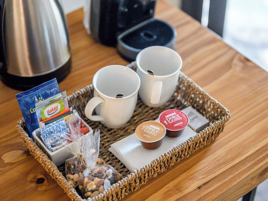 Una bandeja con dos tazas blancas, una cafetera, un hervidor y algunos alimentos sobre una mesa de madera.