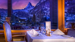 A dining table set with a white tablecloth, wine glasses, and cutlery. A wooden chair is positioned at the table. - Christiania Mountain & Spa (Zermatt)
