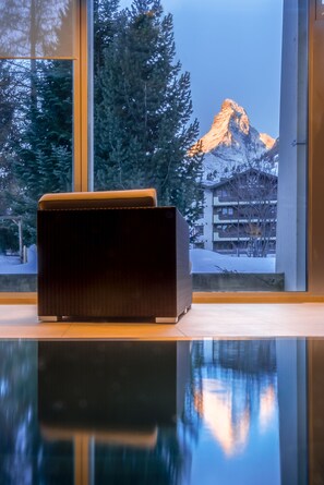 A modern room with a large window offering a view of a mountain and a hotel building. - Christiania Mountain & Spa (Zermatt)