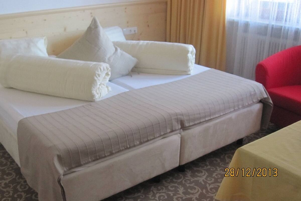 Una habitación de hotel con cama, almohadas, una silla roja y una mesa.