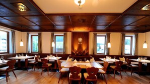 Un restaurante con suelo de madera, mesas y sillas de madera, y ventanas amplias con cortinas.
