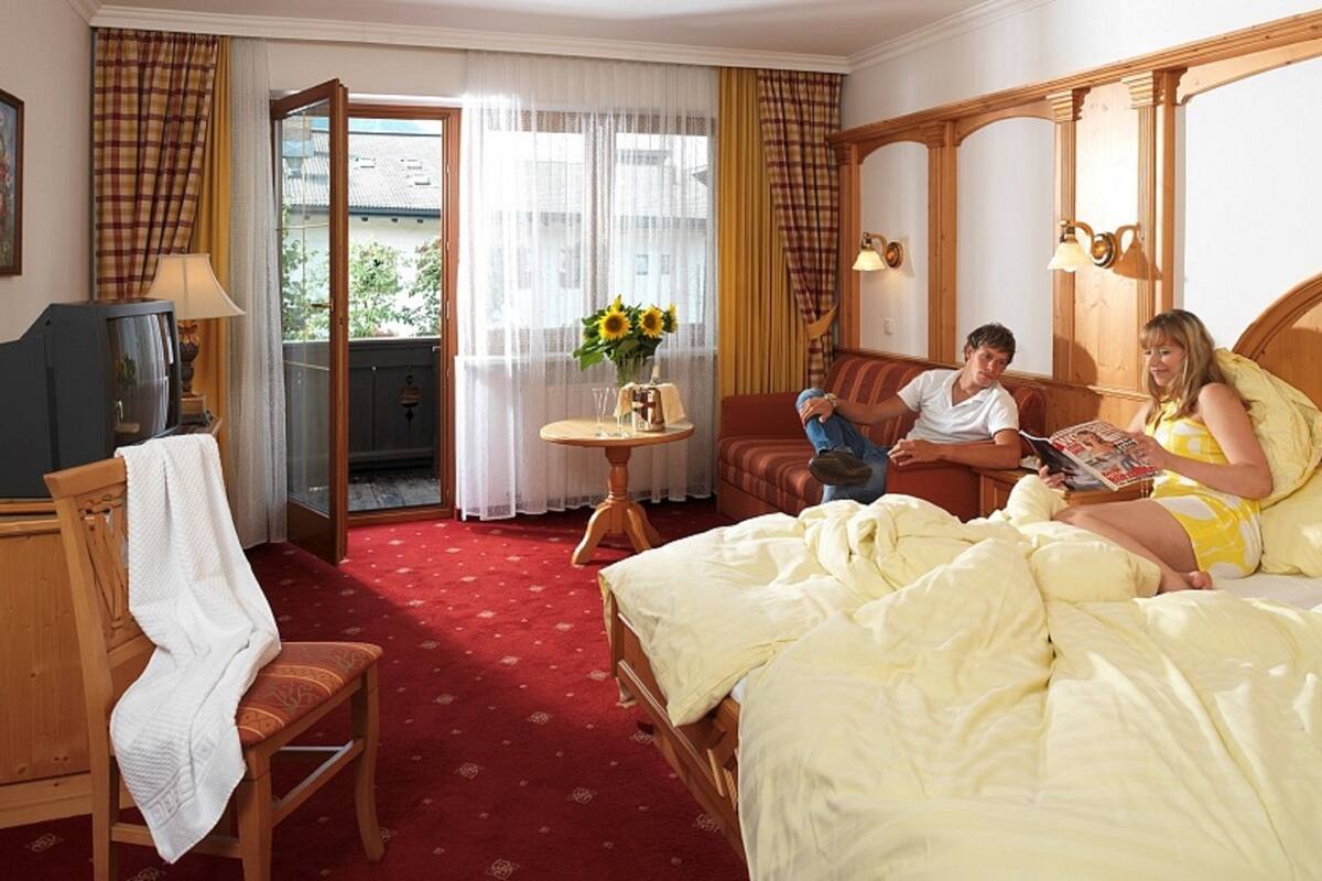 Una habitación de hotel con cama, una silla, una mesita con un jarrón de flores y un televisor.