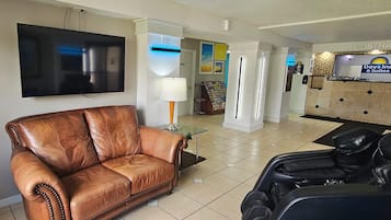 Habitación de hotel con sofá de cuero, sillón de masaje, televisor de pantalla plana, lámpara y un mostrador de recepción con un letrero de Days Inn & Suites.