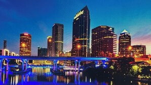 A city skyline with illuminated buildings and a bridge reflecting on the water.