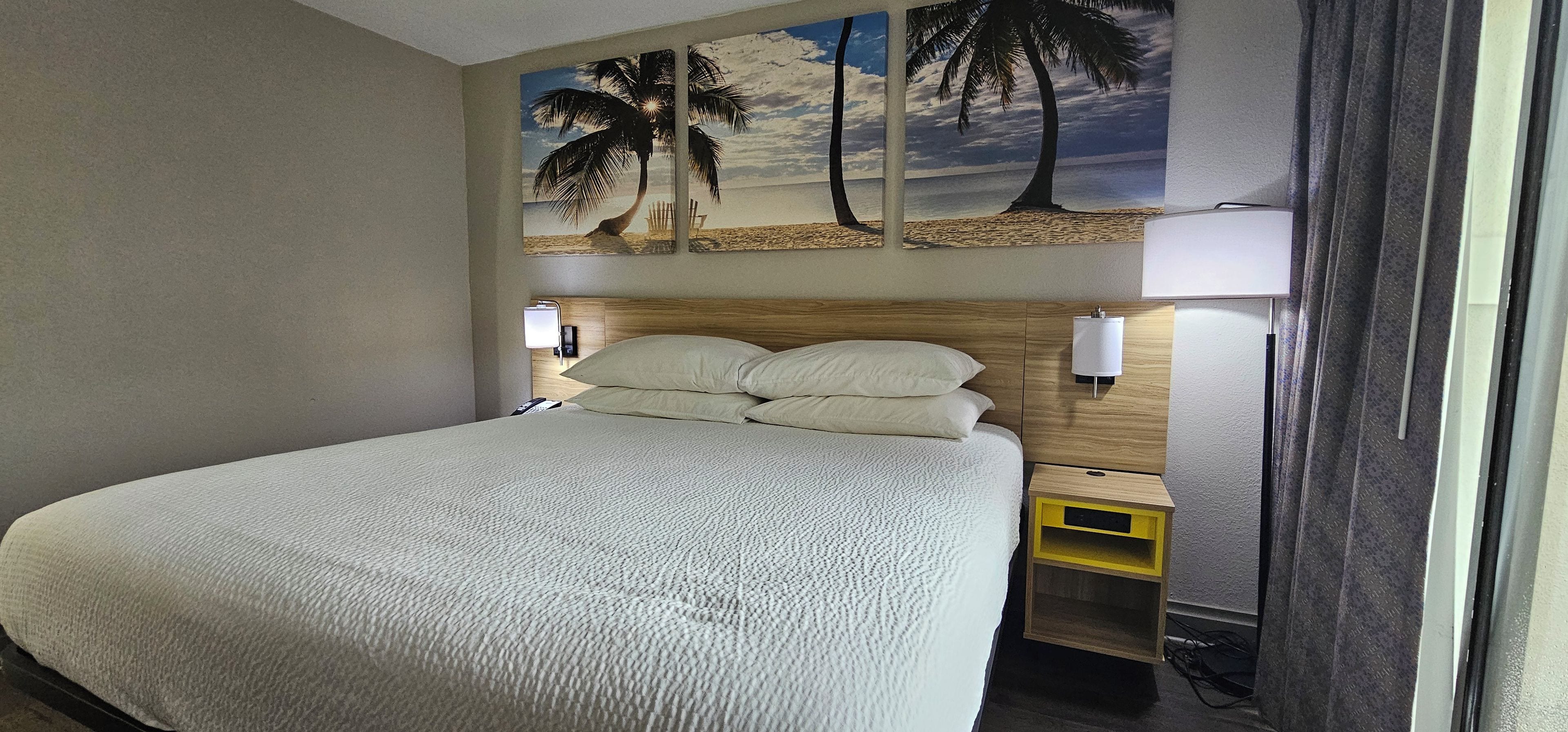 Una habitación de hotel con cama, mesita de noche, lámpara y estante en la pared.