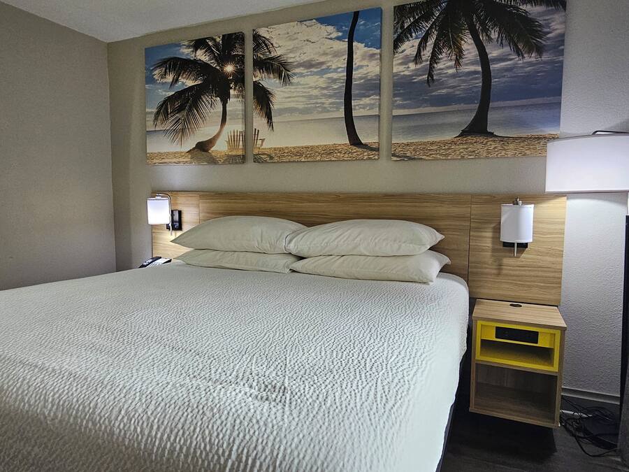 A hotel room with a bed, a nightstand, a lamp, and a wall-mounted shelf.