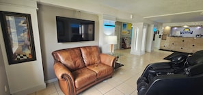Un hall de hotel con un sofá de cuero, un televisor de pantalla plana, un mostrador de recepción y una silla de masaje.