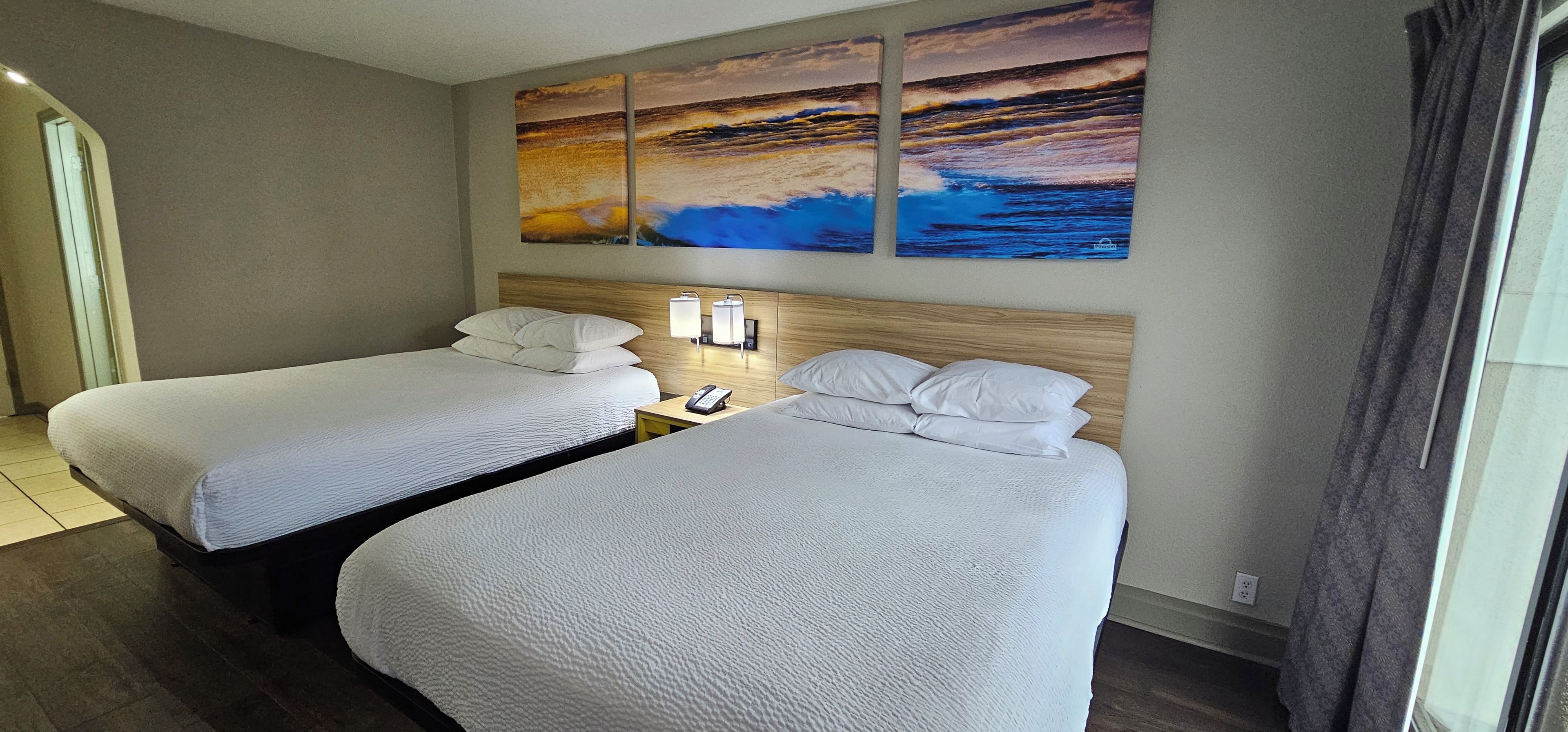 A hotel room with two beds, a nightstand, a phone, and a painting above the beds.