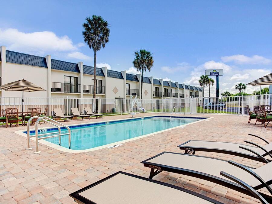 A swimming pool area with lounge chairs, a fence, and a building with a sign for Days Inn & Suites.
