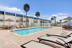 A swimming pool area with lounge chairs, a fence, and a building with a sign for Days Inn & Suites. - Days Inn & Suites by Wyndham Tampa/Fairground/Casino Area (Tampa)