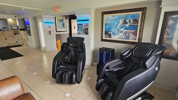 A massage therapy room with two massage chairs, a reception desk, and a painting on the wall.