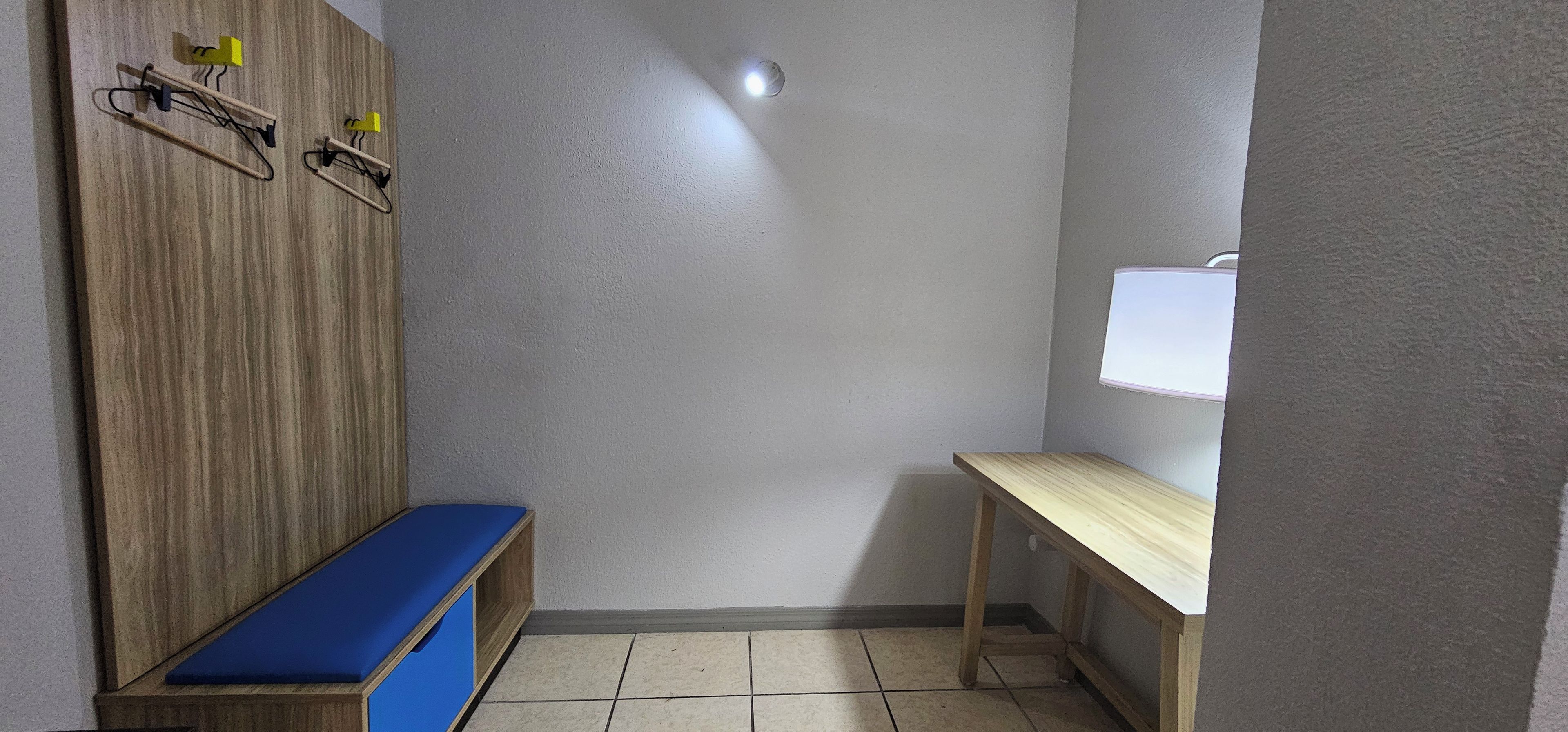 A small room with a wooden bench, a table, and a wall-mounted light fixture.