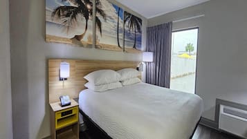Habitación de hotel con una cama grande, una mesita de noche con teléfono, un cuadro de una playa y vistas al exterior.