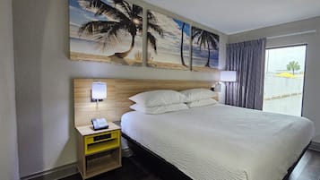 Una habitación de hotel con una cama, una mesita de noche con un teléfono, una lámpara de pared y un cuadro de una playa.