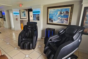 A massage therapy room with two massage chairs, a painting of a coastal scene, and a sign indicating massage services. - Days Inn & Suites by Wyndham Tampa/Fairground/Casino Area (Tampa)