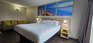 A hotel room with a bed, a sofa, a nightstand, and wall-mounted lights. - Days Inn & Suites by Wyndham Tampa/Fairground/Casino Area (Tampa)