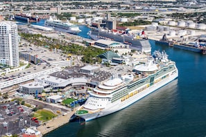 Ein großes Kreuzfahrtschiff liegt an einem Hafen mit einem Yachthafen, Terminalgebäuden und einem Parkplatz.